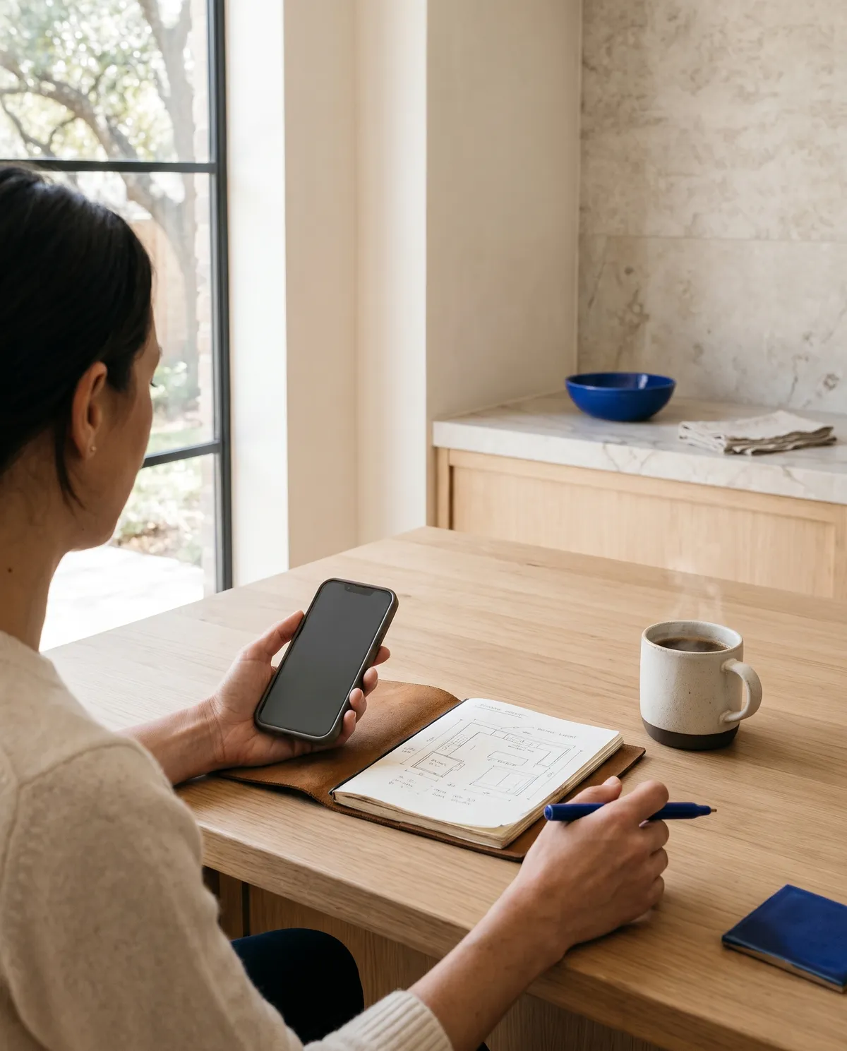 A homeowner on a call with a hand-sketched kitchen layout and coffee on the island (concept rendering)